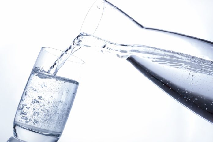 Mineralwasser in Wasserglas einschenken