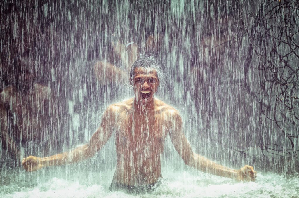 Mann schreit unter Wasserfall